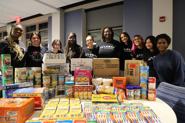 Students stand behind a table displaying donated food and goods for a collection drive