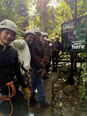 Students wear zip-line gear in front of sign