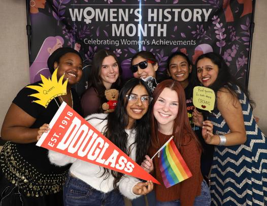 Students pose in front of Women's History Month backdrop